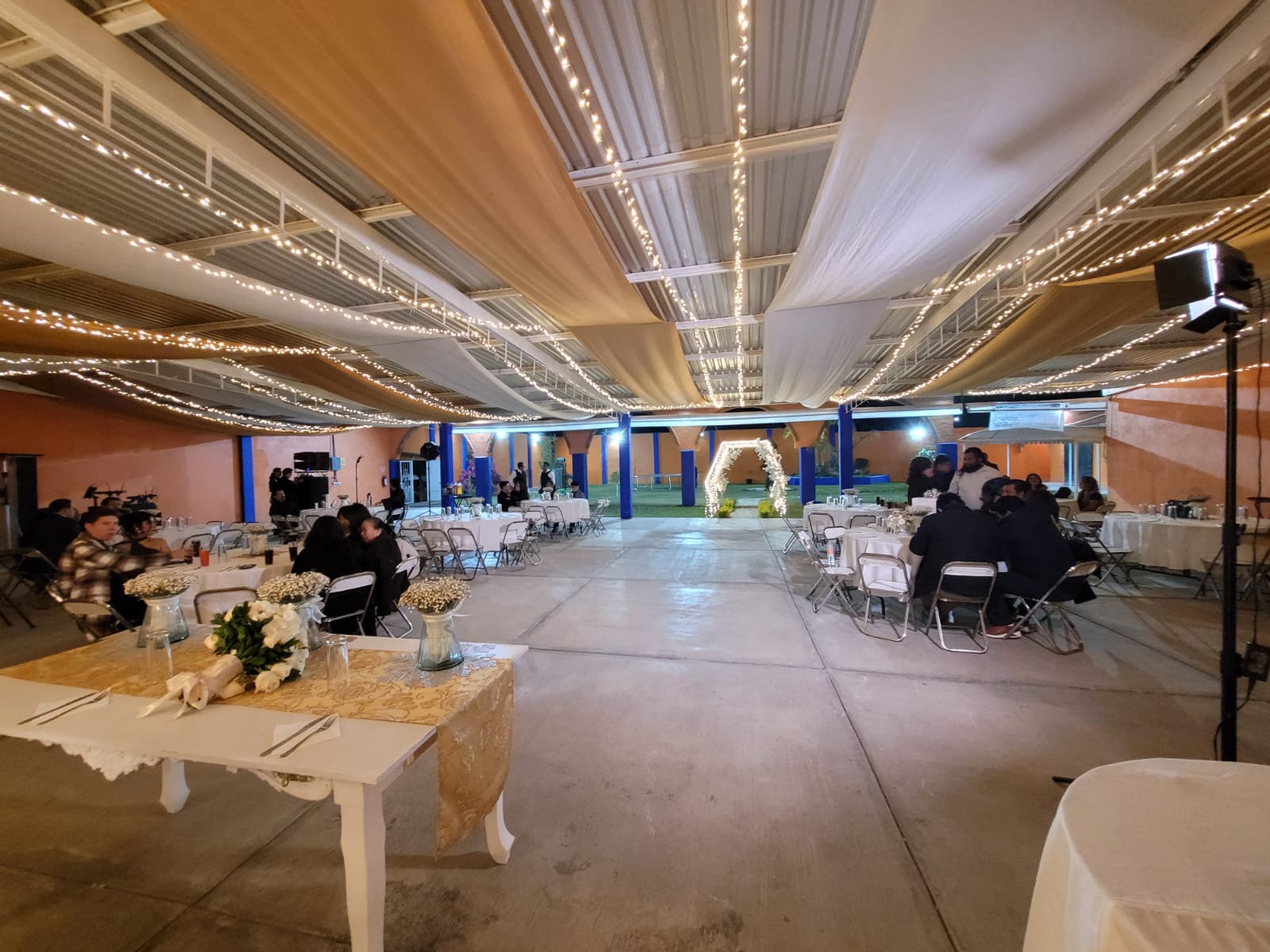 Salón montado de noche para una boda, con luces colgantes y arco iluminado